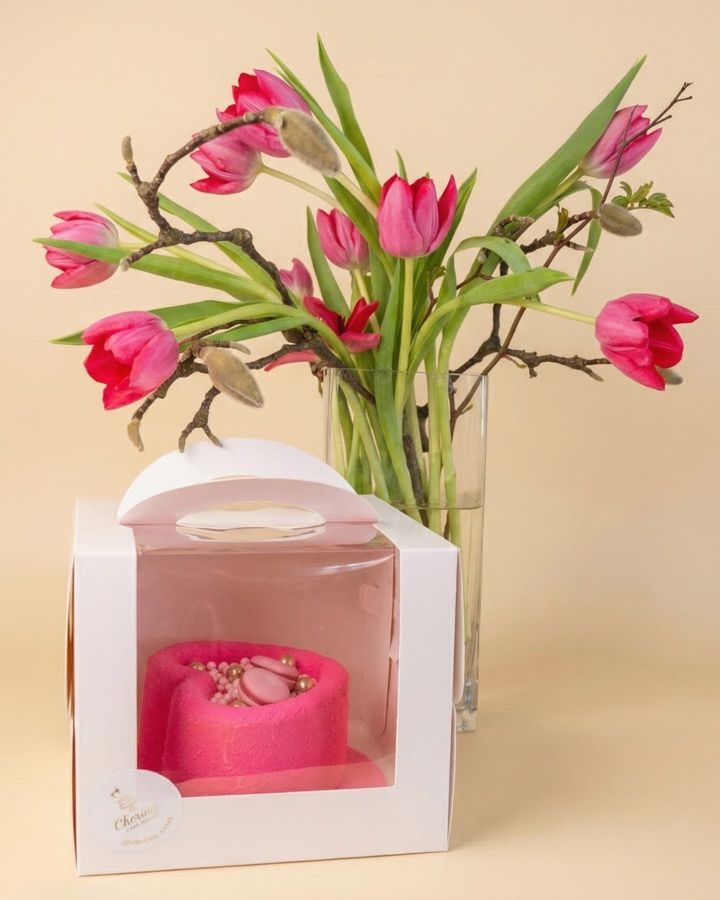 Rosa Herztorte in einer Geschenkbox neben Tulpen